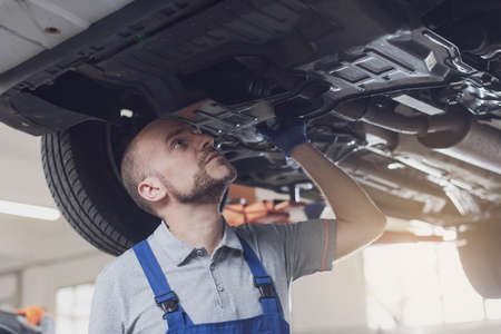 Professional mechanic working under a car in a repair shop, car maintenance and repair conceptの写真素材