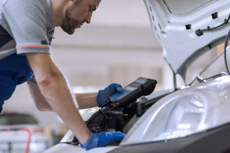 Professional mechanic doing a car inspection, he is using a battery testerの写真素材