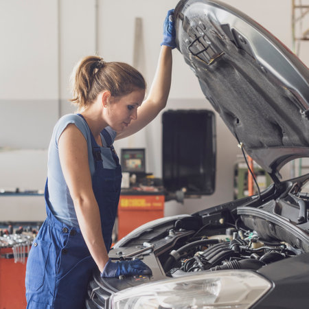 Confident female mechanic working in the auto repair shop, she is checking a car engineの写真素材