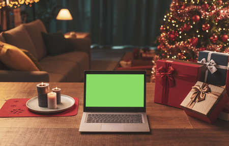 Laptop with blank screen on a table with gifts, Christmas tree in the backgroundの写真素材