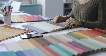 Woman sitting at desk and selecting fabric swatches, she is touching the samples and checking the material, hands close upの写真素材