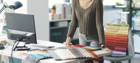 Young creative designer and decorator checking textile samples in her studio, she is picking the...