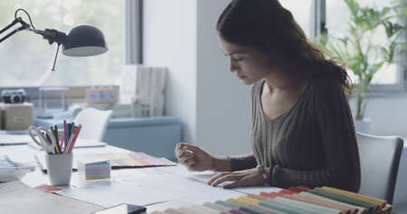 Professional interior designer working in her studio, she is sitting at desk and working on a...