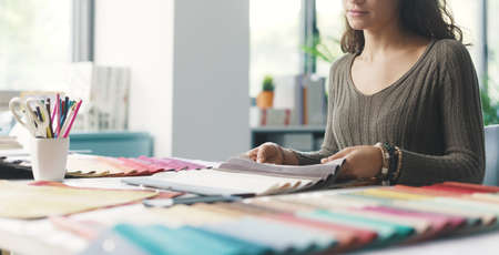Young interior designer sitting at desk and choosing fabric samples for her project