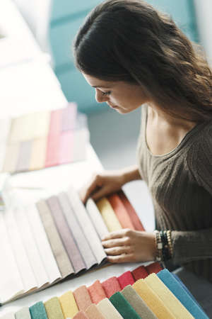 Young interior designer sitting at desk and choosing fabric swatches for her projectの写真素材