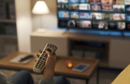 Young woman relaxing on the couch at home and watching videos on demand on her TV, entertainment...