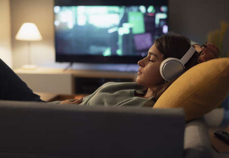 Young woman resting on the couch at home, she is wearing wireless headphones and listening to musicの写真素材
