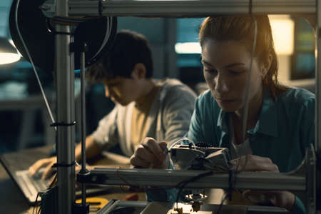 Smart students using a 3D printer and a laptop, engineering and prototyping concept