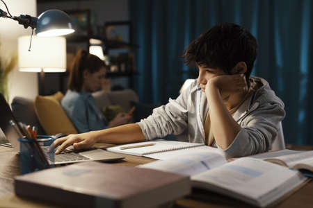 Teenager sitting at desk at home and connecting with his laptop, he is watching online classesの写真素材