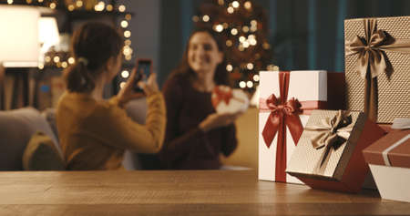 Happy sisters spending time together and taking pictures during holidays, Christmas gifts in the foregroundの写真素材