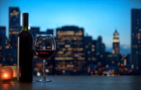 Romantic red wine tasting with candles and city skyline at nightの写真素材