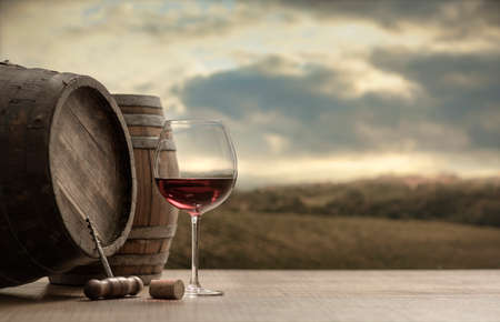 Red wine glass, barrel and corkscrew on a wooden table and vineyard in the backgroundの写真素材