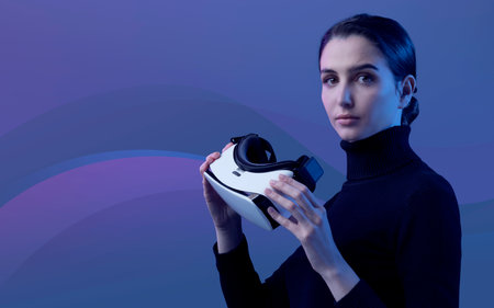 Attractive young woman holding a VR headset and looking at camera, virtual reality and simulated...