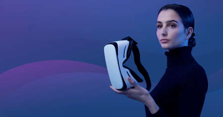 Attractive young woman holding a VR headset and looking away, virtual reality and metaverse concept
