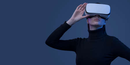 Young beautiful woman wearing a VR headset and experiencing virtual reality, futuristic technology conceptの写真素材