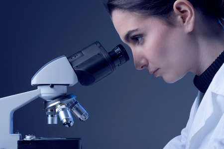 Young researcher looking through a microscope and checking samples, medical research concept