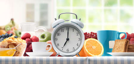 Vintage alarm clock and delicious healthy meal on the kitchen table at homeの写真素材
