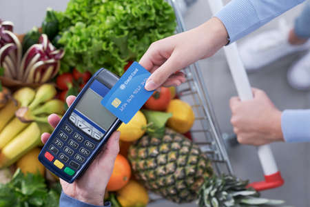 Woman paying for groceries using her credit card, the supermarket cashier is holding the POS terminalの写真素材