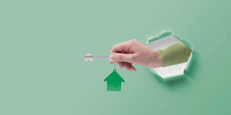 Real estate agent hand in a paper hole holding house keys, real estate conceptの写真素材