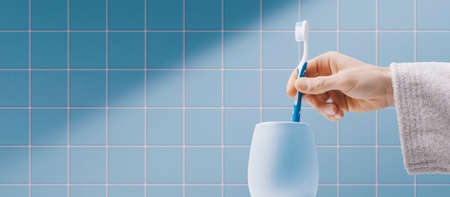 Man cleaning teeth in the bathroom, he is taking his toothbrush in the toothbrush holderの写真素材