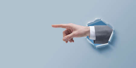 Businessman hand pointing and coming out of a hole in paperの写真素材
