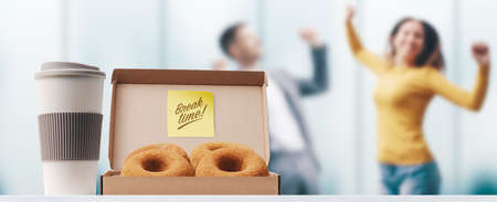 Happy business people taking a break during work hours, coffee and donuts in the foreground