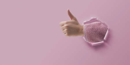 Woman wearing a bathrobe and giving a thumbs up through torn paperの写真素材