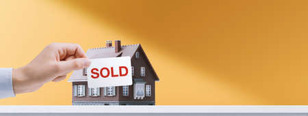 Real estate agent holding a sold sign in front of a model house, successful sale conceptの写真素材