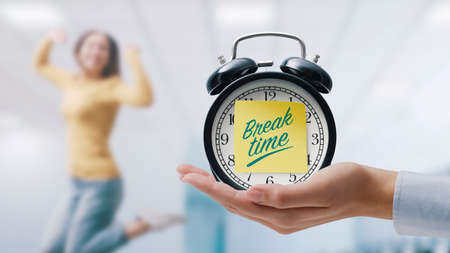Hand showing a vintage clock with sticky note and happy woman jumping and celebrating, it's break timeの写真素材