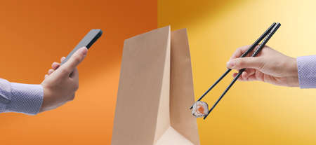 Customer ordering delivery food using her smartphone and eating sushi using chopsticks