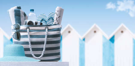 Beach bag with accessories and cabins in the background, summer vacations at the beachの写真素材