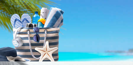 Stylish beach bag with accessories and tropical beach in the background, summer vacations conceptの写真素材