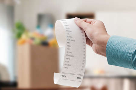 Woman checking a grocery receipt and bag full of groceries in the backgroundの写真素材