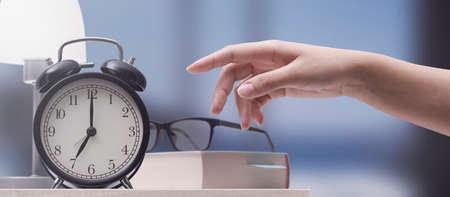 Woman turning off a vintage alarm clock, she wakes up early
