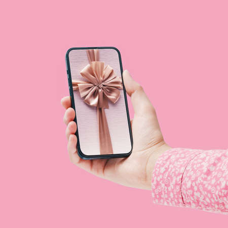 Woman holding a smartphone with a gift ribbon on the display, she is receiving a beautiful virtual...