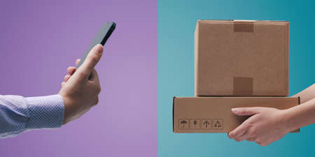 User ordering products online using a smartphone and courier carrying delivery boxes: e-commerce and online shopping conceptの写真素材