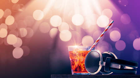 Delicious cocktail and headphones on a table at the dance club, bokeh disco lights in the...