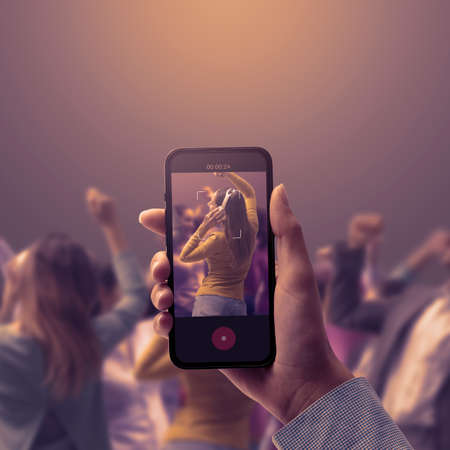 Woman holding a smartphone and shooting a video of people dancing at the party