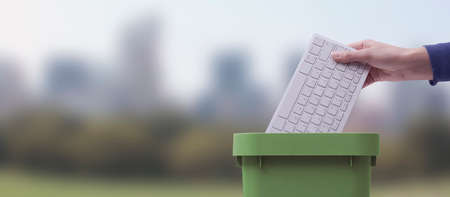 Woman putting a computer keyboard in the trash bin, e-waste recycling concept, natural landscape in the backgroundの写真素材