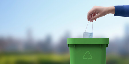 Woman putting an used face mask in the trash bin, medical waste disposal conceptの写真素材