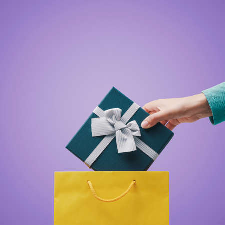 Woman putting a gift box with ribbon in a shopping bag, copy spaceの写真素材