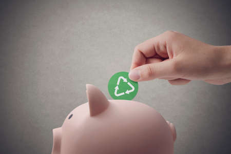 Woman putting a coin with recycling symbol in a piggy bank, green investing conceptの写真素材