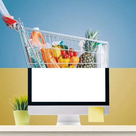 Online grocery shopping: computer and shopping cart full of groceries