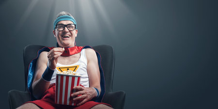 Funny happy superhero watching comedy movies and eating popcorn, he is staring at the screen and laughingの写真素材