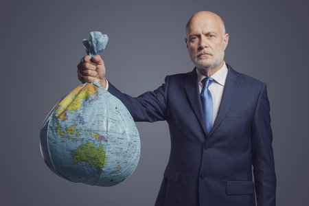 Corporate businessman holding a polluted damaged earth, the globe is shaped as a trash bagの写真素材