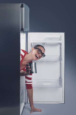 Funny smiling woman inside the fridge, she has found canned foodの写真素材