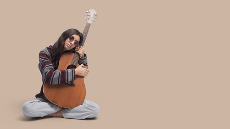 Stylish hippie woman sitting with legs crossed and holding an acoustic guitar, music and inspiration conceptの写真素材