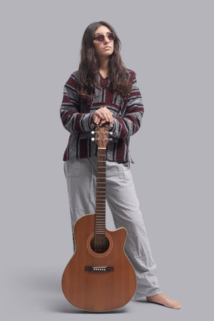 Young hippie woman standing and holding her acoustic guitar, full-length portrait