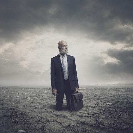 Businessman trapped in a dry desert land, he is lost and hopeless, crisis and environmental damage conceptの写真素材