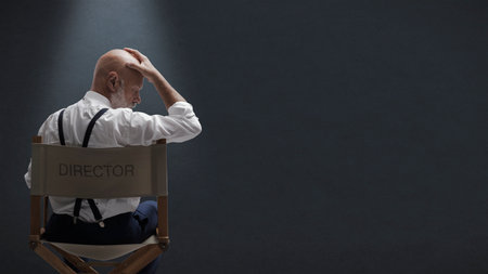 Disappointed filmmaker sitting on the director's chair and touching his head, he is stressed and...
